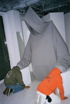 Two children, one in a green hoodie and one in orange, are crouched on the floor, each holding a large white cube, as if building or playing with a giant structure.