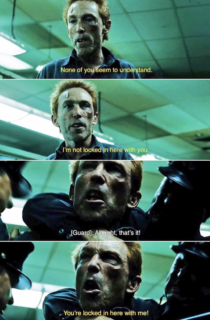 A man with bloodied and bruised face, wearing a dark shirt, is being forcibly held by guards in a dimly lit, green-tinted room. He screams, “You’re locked in here with me!” as the guards respond with “All right, that’s it!” The scene conveys intense struggle and confinement.